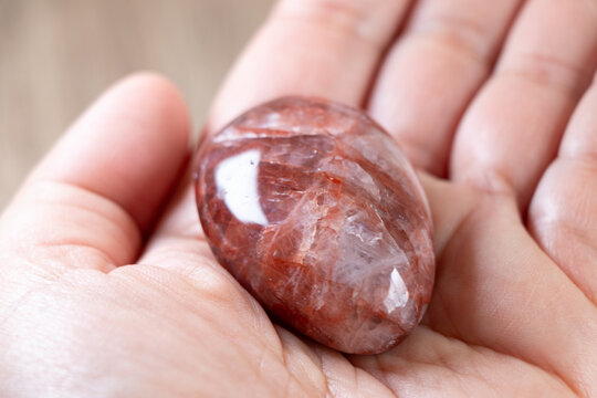 Piedra de cuarzo con inclusiones de hierro, llamada cuarzo fuego, textura pulida, una mano la sostiene para mostrar sus caracter&iacute;sticas.