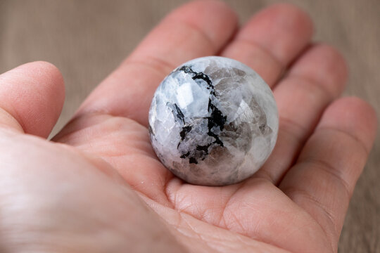 primer plano de una esfera de piedra luna natural perfectamente pulida y brillante, descansando delicadamente sobre la palma de una mano.