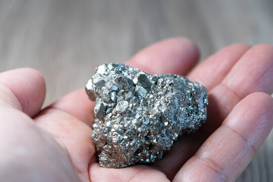 Piedra Pirita natural sobre la palma de una mano, primer plano de mineral plateado dorado brillante, s&iacute;mbolo de abundancia, energ&iacute;a y protecci&oacute;n.