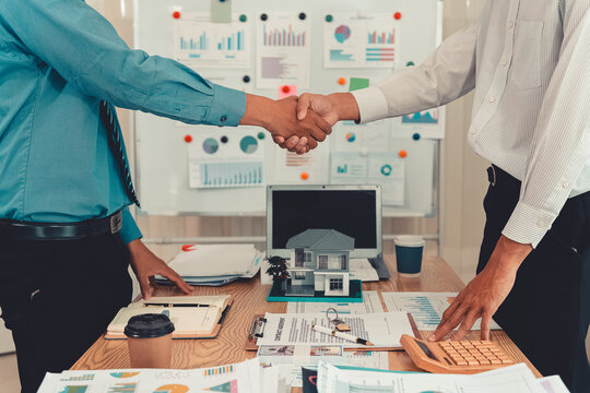 Real estate agent shaking hands with client after signing contract agreement for buying house.
