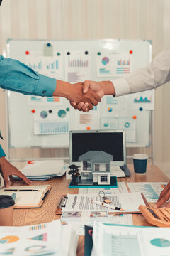 Real estate agent shaking hands with client after signing contract agreement for buying house.