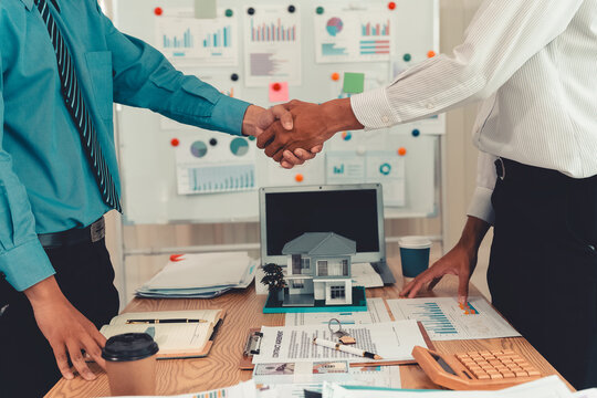 Real estate agent shaking hands with client after signing contract agreement for buying house.