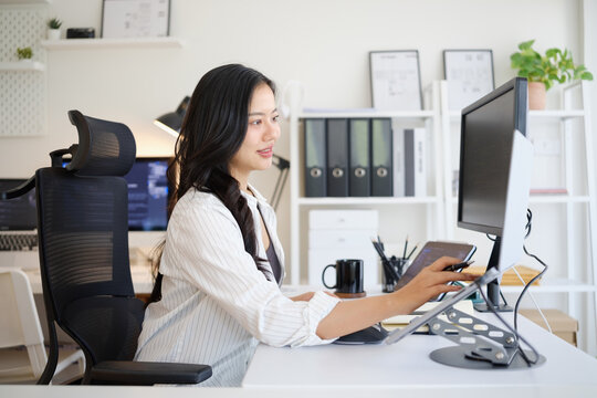 Female programmer writing code on multiple computer screens at a modern office workstation.