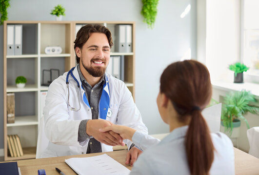 Doctor and patient shake hands during consultation, hospital meeting. Smiling happy physician greeting woman with handshake to welcome before professional medical checkup, quality care in clinic