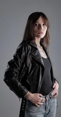 Young woman looking at camera, wearing a black leather jacket and jeans in a studio © 4kclips