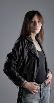 Young woman looking at camera, wearing a black leather jacket and jeans in a studio