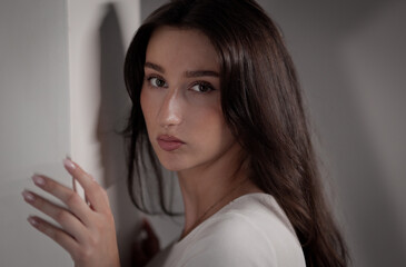 Fototapeta premium Young woman posing with natural makeup, dark hair, and subtle shadows on a studio wall
