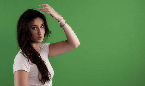 Young woman posing in a studio against a green background, looking at the camera