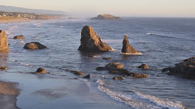 Waves roll gently on to Oregon Coast beach in Bandon at sunset with sea stacks