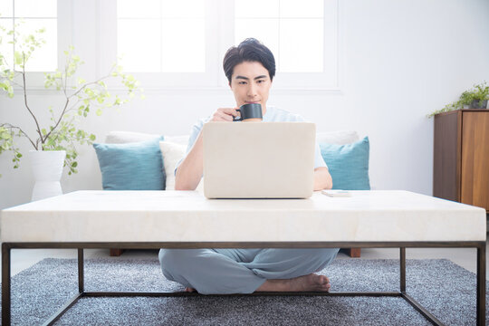ノートパソコンで仕事や検索ををする日本人男性　自宅でコーヒーを飲みながらテレワークやリラックスをするライフスタイル全身