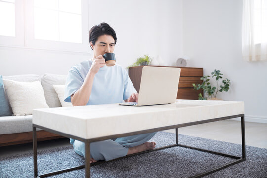 ノートパソコンで仕事や検索ををする日本人男性　自宅でコーヒーを飲みながらテレワークやリラックスをするライフスタイル全身