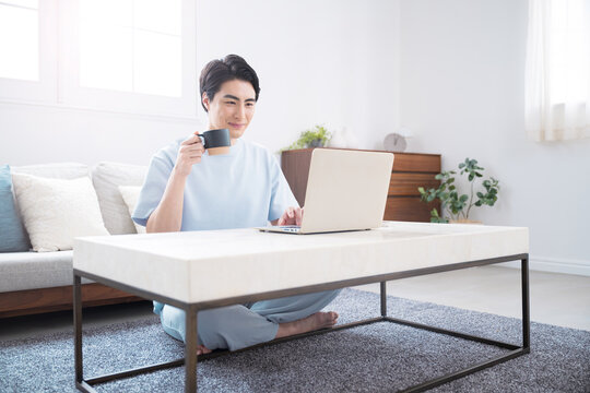 ノートパソコンで仕事や検索ををする日本人男性　自宅でコーヒーを飲みながらテレワークやリラックスをするライフスタイル全身