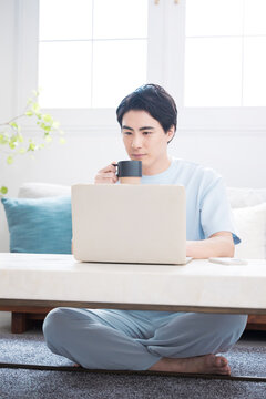 ノートパソコンで仕事や検索ををする日本人男性　自宅でコーヒーを飲みながらテレワークやリラックスをするライフスタイル全身