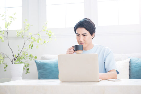 ノートパソコンで仕事や検索ををする日本人男性　自宅でコーヒーを飲みながらテレワークやリラックスをするライフスタイル上半身