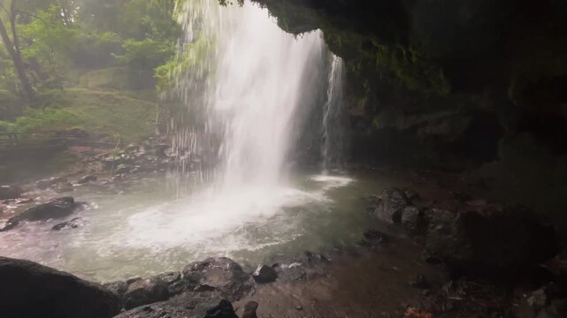 4K view of El Beso waterfall cascading into a natural pool as captured from the dark rocky interior of a hidden cave in the Arcoiris Waterfalls, Honey, Puebla, Mexico.