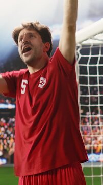Vertical frame: Football celebration after match winning goal as goal scorer raises arms, smiling and celebrating with clenched fists, excitement on pitch after final whistle, winning soccer game.