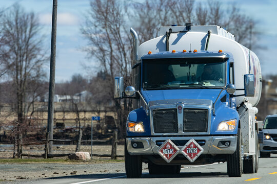 Quebec, Canada, 24 April 2026 : A blue Kenworth tanker truck transports hazardous materials on a road under a clear sky.