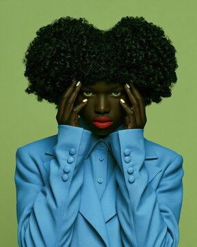 Young African woman with afro pigtails wearing a sky blue blazer against a green background for fashion and youth culture