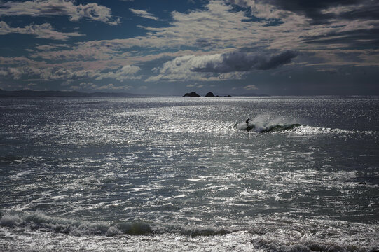 A lone surfer gracefully rides a shimmering wave under a dramatic, cloudy sky during a tranquil afternoon. - horizontal