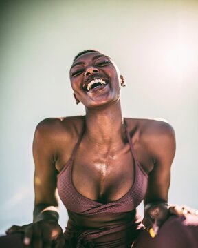 Joyful Black woman laughing during a vigorous workout, featuring glowing perspiring skin and a triumphant mood for fitness and athletic apparel