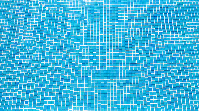 Clear blue water ripple in swimming pool with mosaic tiles background under sunlight.
