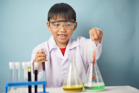 Smiling young boy wearing protective goggles and a lab coat while conducting a colorful chemistry experiment using laboratory glassware. STEM learning and scientific exploration concept.