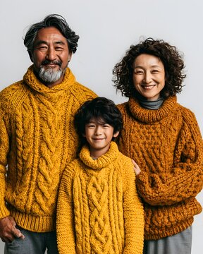 Joyful Asian family portrait featuring father, mother, and son in matching warm cable knit sweaters, smiling happily at the camera