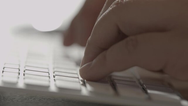 A close-up of a person's hand typing on a white keyboard with fingers on the keys in a bright minimal workspace.
