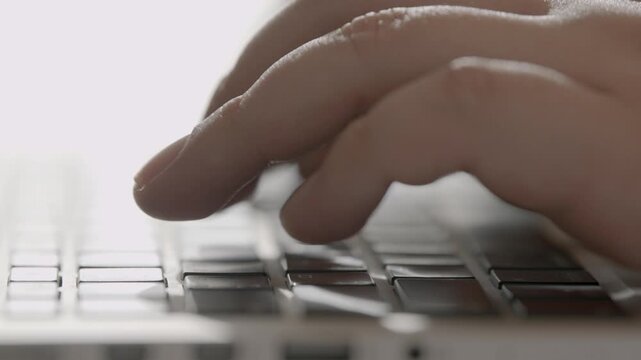 A close-up side view of a person's fingers pressing keys on a white keyboard in a bright minimal office setting.