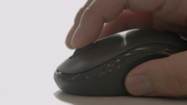 A close-up of a person's hand holding and using a dark wireless computer mouse on a desk surface.