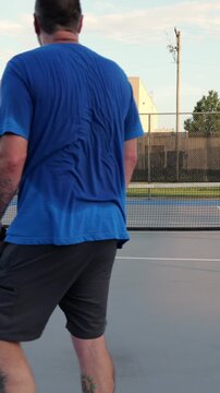 Middle-aged man and woman playing recreational pickleball match hitting yellow ball and shaking hands over the net on a sunny day at community park