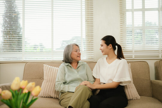 Senior woman and young caregiver enjoying a warm conversation on a sofa at home, highlighting compassionate elderly care and family support.
