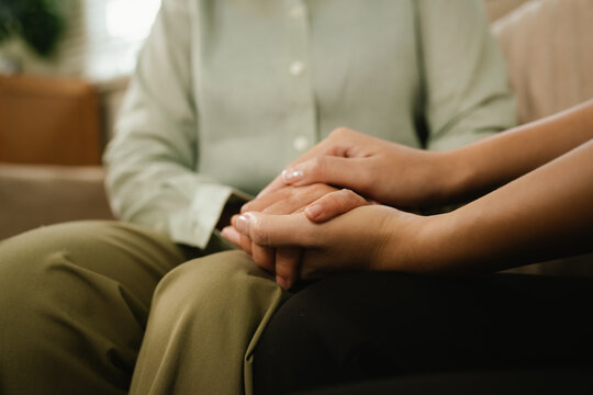 Close-up of a caregiver holding a senior woman's hands, expressing compassion, comfort, trust, and emotional support at home.