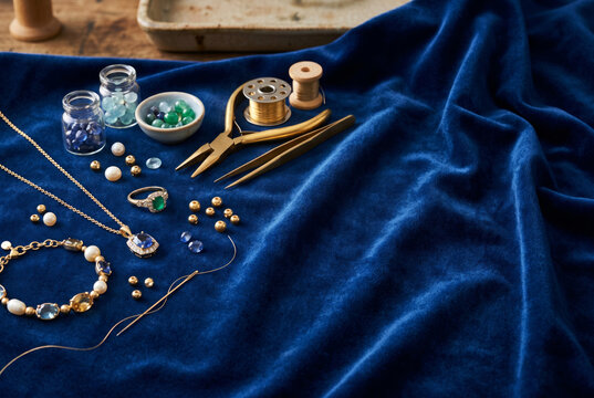 Handmade jewelry, decorative beads and gold crafting tools arranged on luxurious velvet fabric for artisan inspired designs. Jewelry making and craftsmanship concept. Copy space
