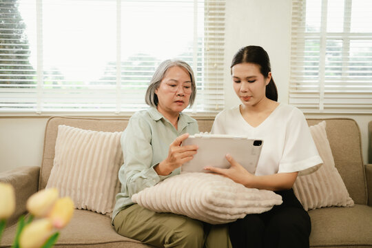 Senior woman and young caregiver using a tablet together at home, promoting digital inclusion, technology learning, and elderly support.