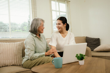 Fototapeta premium Senior woman and young caregiver using a laptop together at home, promoting digital inclusion, family support, and elderly technology learning.