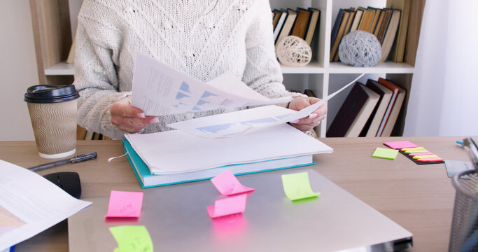 Office paperwork. Business lifestyle. Unrecognizable female professional preparing for work at desk with notebook laptop at workplace.