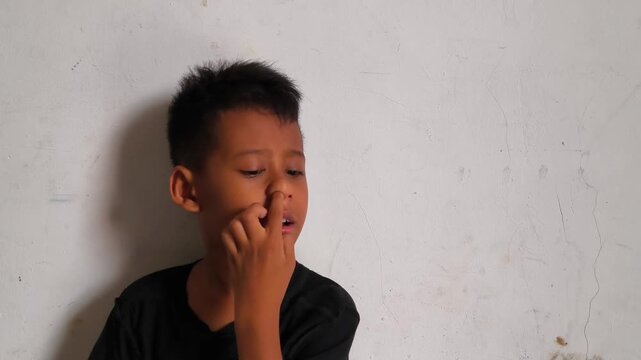 Close up of a cute young boy making various funny facial expressions, gestures, and posing for the camera against a neutral background.