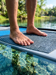 Fototapeta premium Low Angle View of Feet Standing on Paddleboard in Transparent Lake