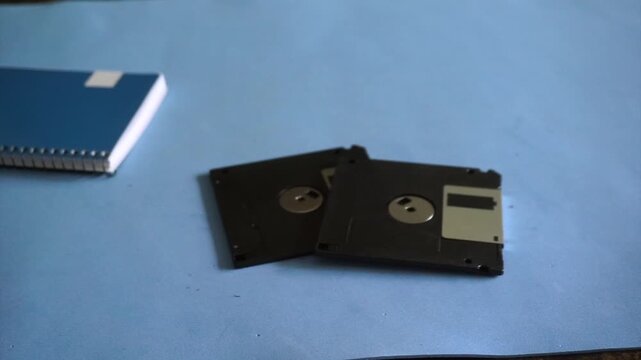 Hands placing two old 3.5 inch floppy disks for data storage on a blue desk