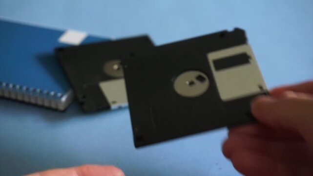 Male hands holding and dropping two vintage 3.5 inch floppy disks on a blue office desk