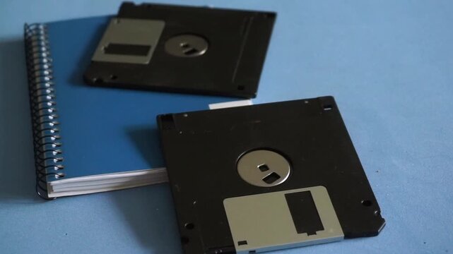 Man's hand using an old floppy disk as a bookmark on a notebook, concept of obsolete technology