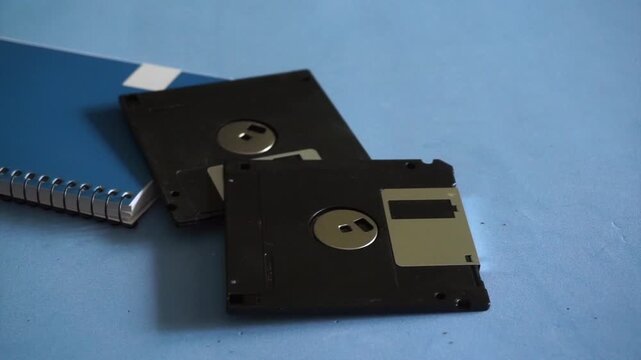 Human hand putting several vintage 3.5 inch floppy disks on a blue desk next to a notebook