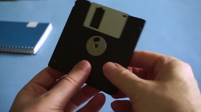 Person holding a retro black floppy disk in hands, showing an obsolete data storage medium
