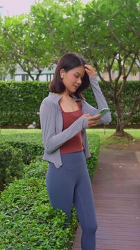 Asian sporty woman wear earphone using smartphone standing in park.