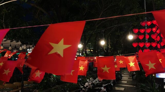 Close up of small Vietnamese Flags above Night alley. Holidays Celebration Scene