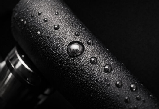 Artistic black and white macro photograph showing clear condensed water droplets resting on a bicycle handlebar grip