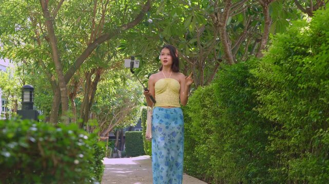Asian woman in swimsuit using selfie stick hold smartphone live streaming on social platform in park