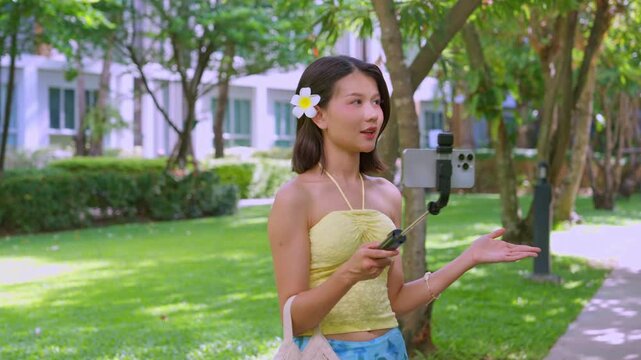 Asian woman in swimsuit using selfie stick hold smartphone live streaming on social platform in park