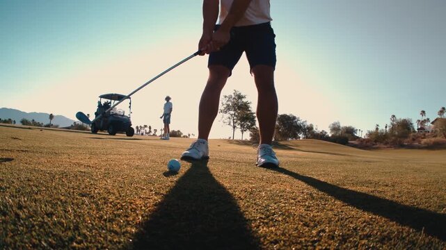 A golfer hits a backlit chip shot spraying mud and grass divot through golden sunset light on a desert course in slow motion, wide angle 4k 800fps